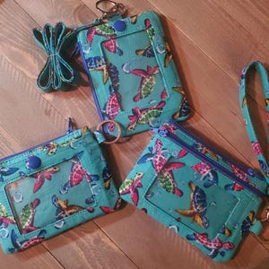 May include: Three turquoise blue fabric zippered pouches with a clear plastic window. Each pouch has a different design of colorful sea turtles. The pouches have a key ring attached.