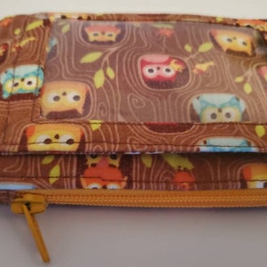 May include: A brown fabric zippered pouch with a clear plastic window. The pouch has a repeating pattern of owls on a brown background. The pouch has a key ring attached to it.