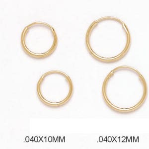 Puede incluir: Un conjunto de pendientes de aro dorados de varios tamaños, sobre un fondo blanco. Los tamaños están etiquetados como .040x10MM, .040x12MM y .040x14MM. Los aros tienen un diseño sencillo y clásico.