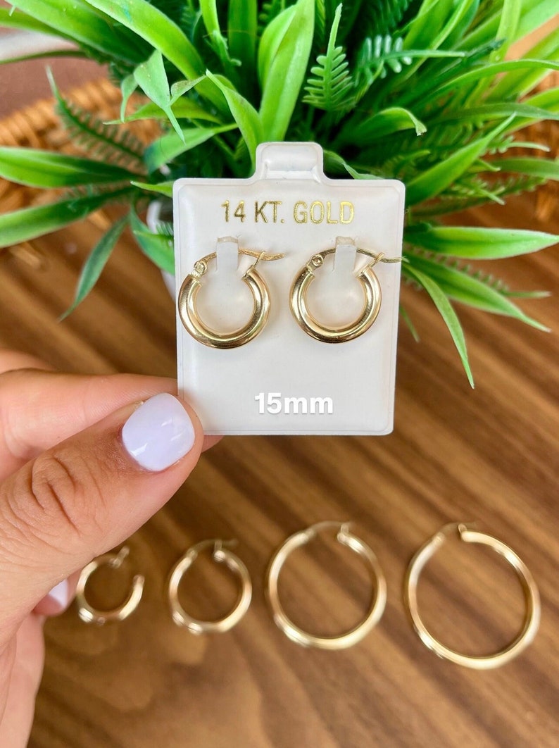 Puede incluir: Un par de pendientes de aro de oro de 14 quilates en una tarjeta blanca con el texto "14 KT. GOLD" y "15mm". Los pendientes tienen un di&aacute;metro de 15 mil&iacute;metros.