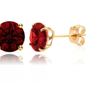 May include: A pair of gold stud earrings with a red gemstone in the center. The earrings have a simple design and are perfect for everyday wear.