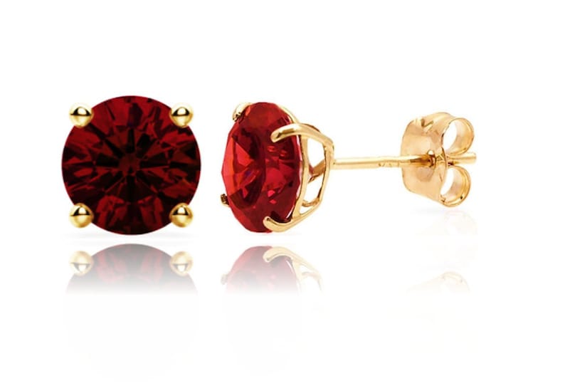 May include: A pair of gold stud earrings with a red gemstone in the center. The earrings have a simple design and are perfect for everyday wear.