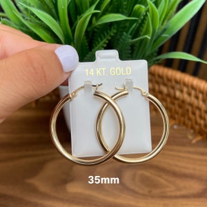 Puede incluir: Un par de pendientes de aro de oro de 14 quilates, de 35 mm de di&aacute;metro. Los pendientes est&aacute;n en una tarjeta blanca con el texto "14 KT. GOLD" y "35mm".