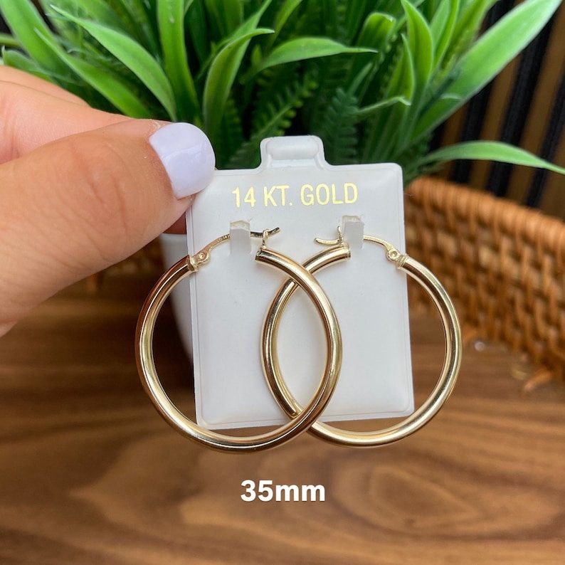 Puede incluir: Un par de pendientes de aro de oro de 14 quilates, de 35 mm de di&aacute;metro. Los pendientes est&aacute;n en una tarjeta blanca con el texto "14 KT. GOLD" y "35mm".