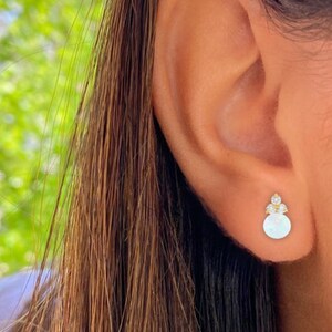 May include: Gold stud earrings with a small round white opal stone and three small clear cubic zirconia stones.