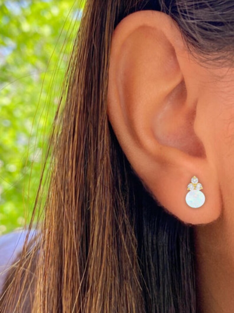 May include: Gold stud earrings with a small round white opal stone and three small clear cubic zirconia stones.