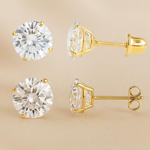 May include: A pair of round, clear gemstone stud earrings with gold-colored settings and posts. The earrings are displayed in two different orientations, showcasing the sparkling facets of the gemstones and the details of the gold backing.