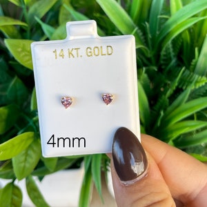May include: A pair of 14 karat gold heart-shaped stud earrings with pink stones. The earrings are 4mm in size and are displayed on a white card.