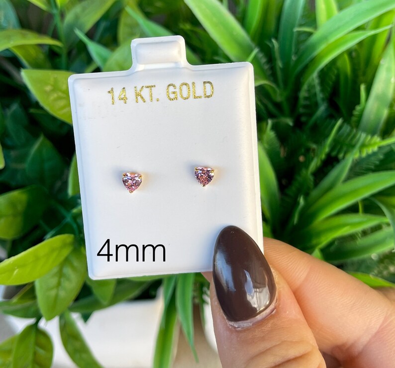May include: A pair of 14 karat gold heart-shaped stud earrings with pink stones. The earrings are 4mm in size and are displayed on a white card.