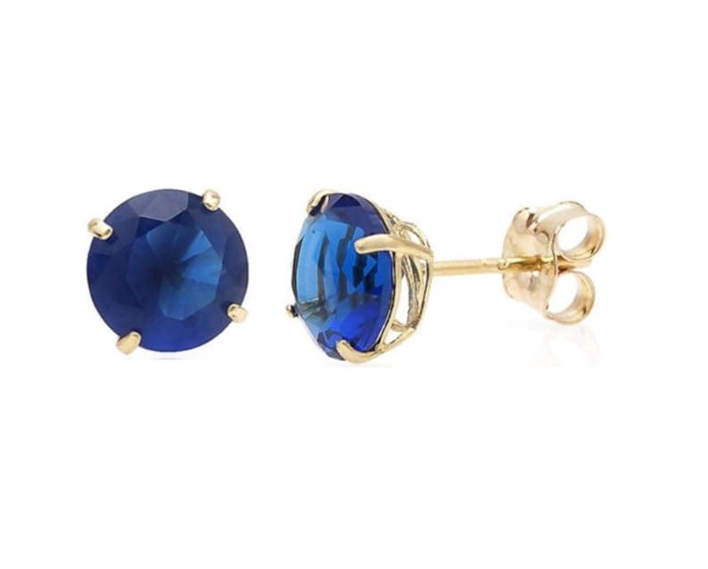 May include: A pair of gold stud earrings with a round blue gemstone in each earring.
