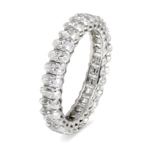 May include: A silver band ring with a row of oval-shaped clear gemstones set in a continuous line around the band.