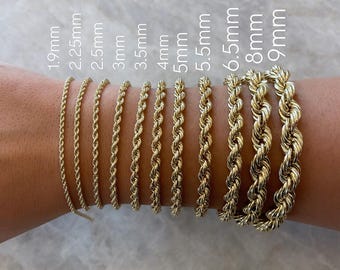 May include: A close-up of a person's wrist wearing ten gold rope chain bracelets of varying widths, ranging from 1.9 mm to 9 mm. The bracelets are arranged in order of size, with the smallest bracelet on the left and the largest bracelet on the right.