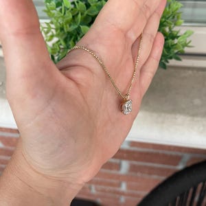 May include: A gold chain necklace with a clear emerald-cut gemstone pendant.