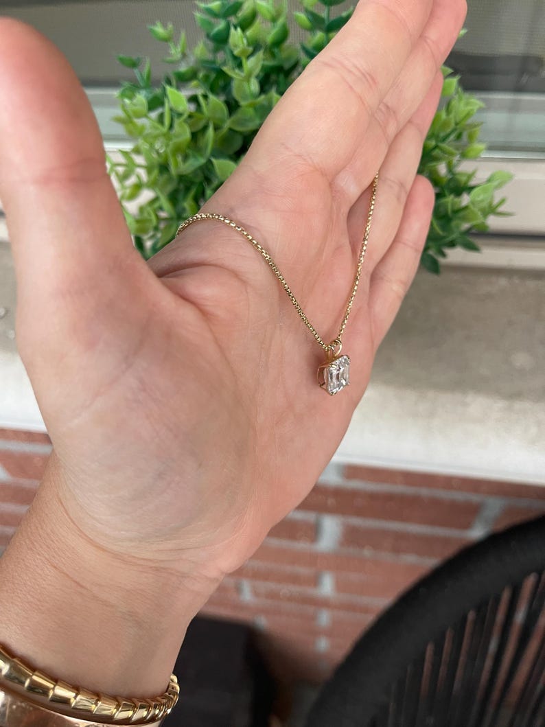 May include: A gold chain necklace with a clear emerald-cut gemstone pendant.