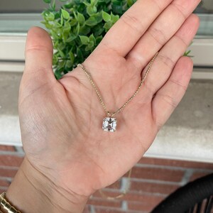 May include: A gold chain necklace with a square-shaped clear gemstone pendant.