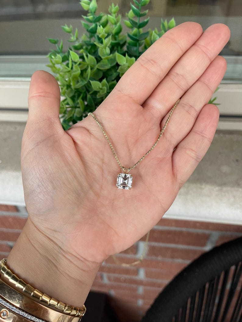 May include: A gold chain necklace with a square-shaped clear gemstone pendant.