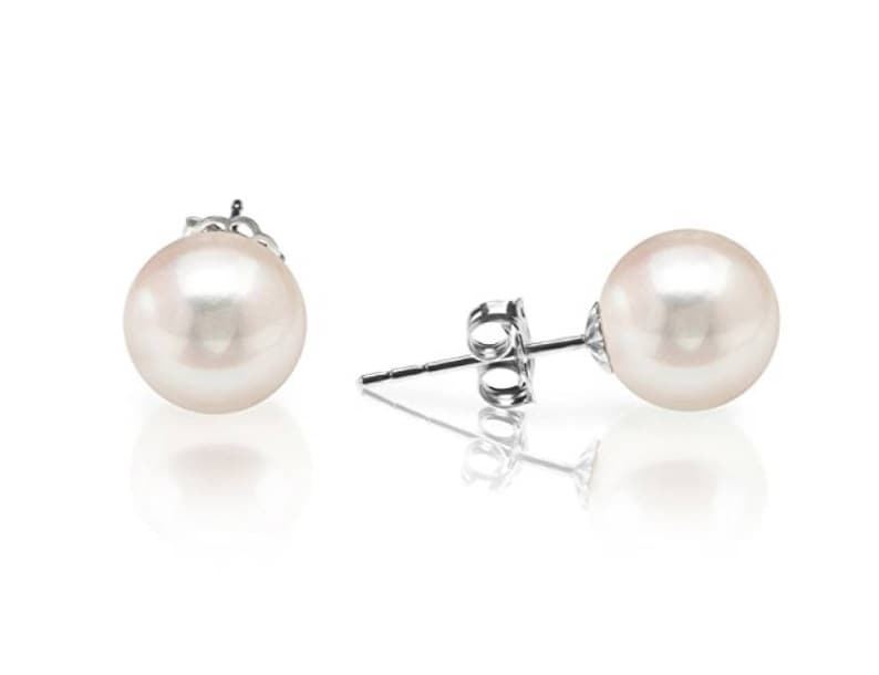 May include: A pair of pearl stud earrings. Each earring features a round, lustrous, off-white pearl set on a silver post with a butterfly backing. The earrings are displayed on a white background with a soft reflection.