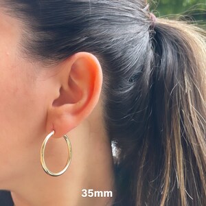 Puede incluir: Pendientes de aro de oro de 35 mm de di&aacute;metro. Los pendientes se muestran en la oreja de una persona.