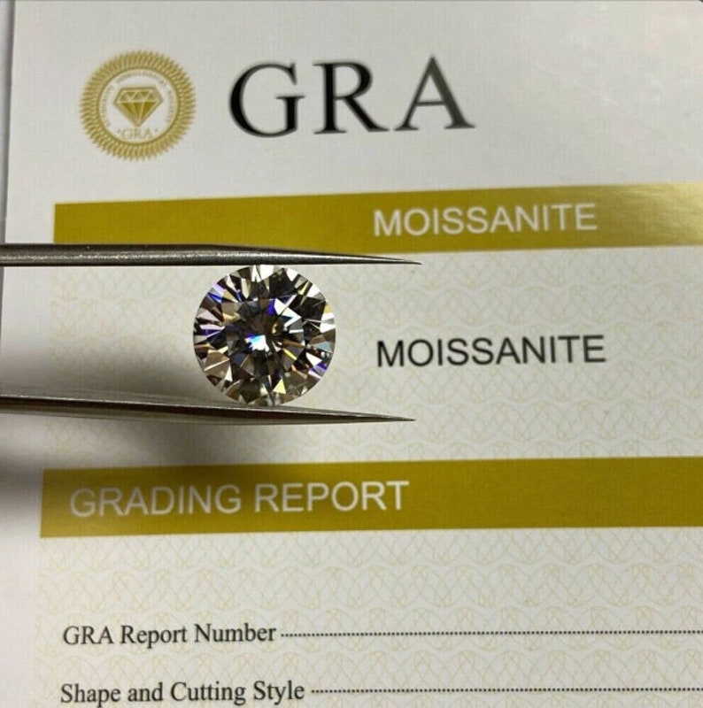 May include: A grading report for a round, clear, colorless, faceted gemstone. The report is labeled "GRA" and "Moissanite".
