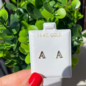 Könnte beinhalten: Ein Paar 14 Karat Gold Ohrringe mit dem Buchstaben "A" besetzt mit kleinen Diamanten. Die Ohrringe werden auf einer weißen Karte mit dem Text "14 KT. GOLD" präsentiert.