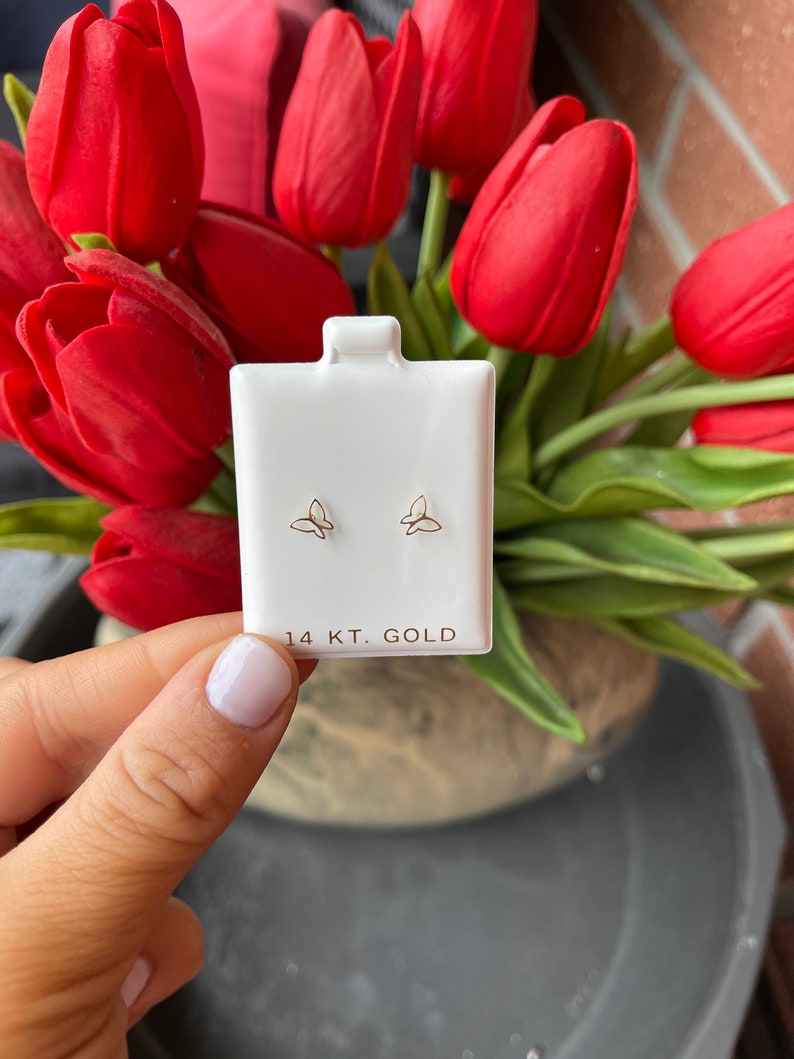 K&ouml;nnte beinhalten: Ein Paar kleine goldene Schmetterlings-Ohrringe auf einer wei&szlig;en Karte mit dem Text "14 KT. GOLD".
