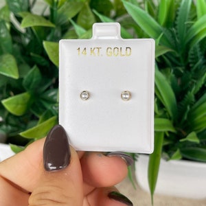 Op de afbeelding: Een paar kleine parel oorbellen met een gouden zetting. De oorbellen worden getoond op een witte kaart met de tekst "14 KT. GOLD".