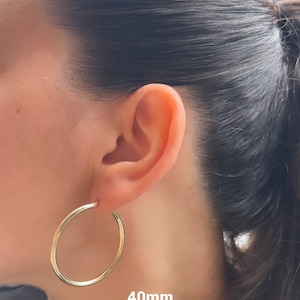 Puede incluir: Pendientes de aro de oro de 40 mm de di&aacute;metro. Los pendientes se muestran en la oreja de una persona.