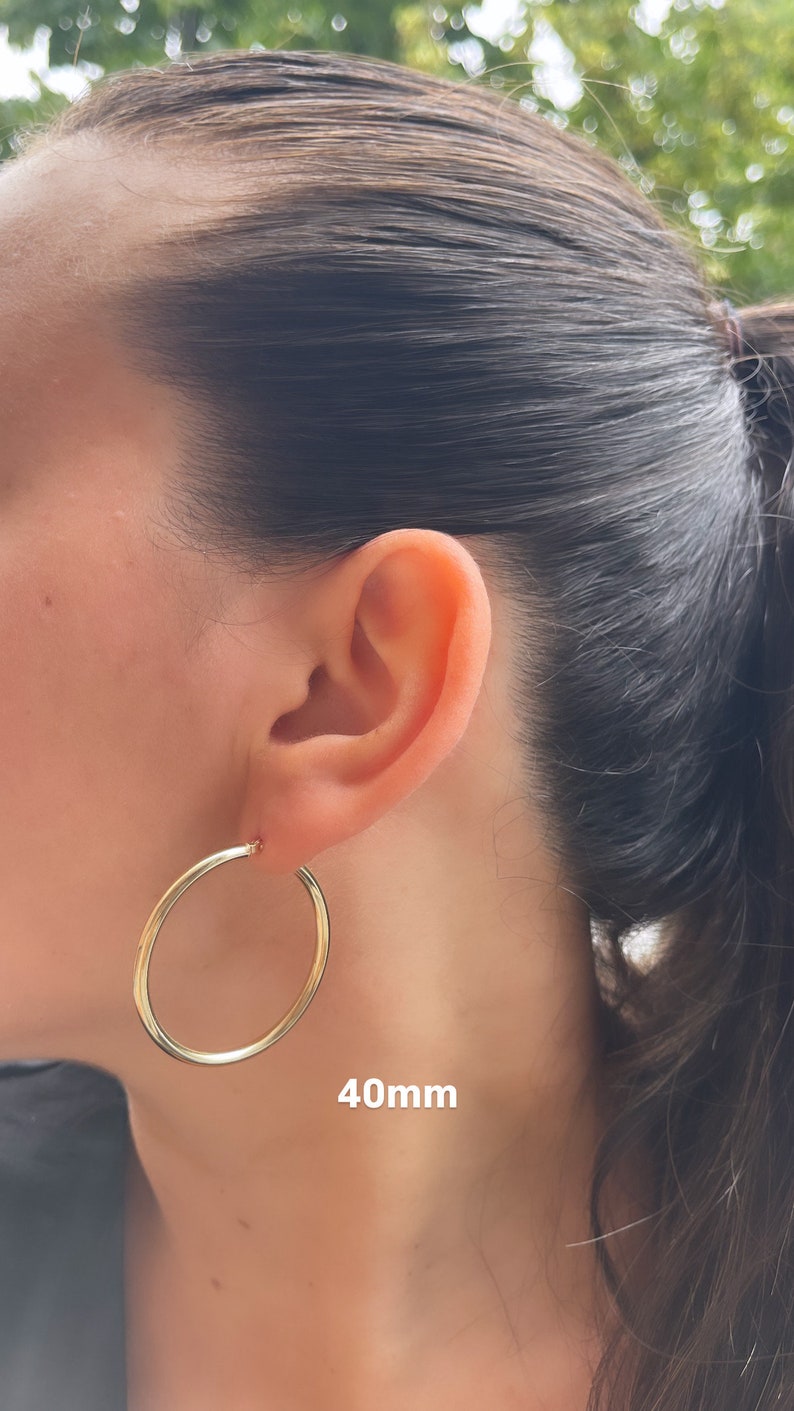 Puede incluir: Pendientes de aro de oro de 40 mm de di&aacute;metro. Los pendientes se muestran en la oreja de una persona.
