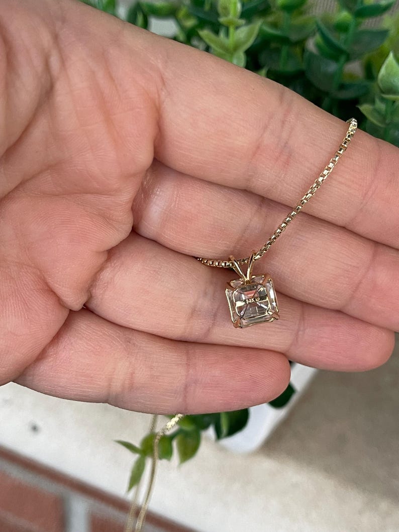 May include: A gold chain necklace with a square-shaped pendant featuring a clear gemstone. The pendant has the inscription "14K" on the back.