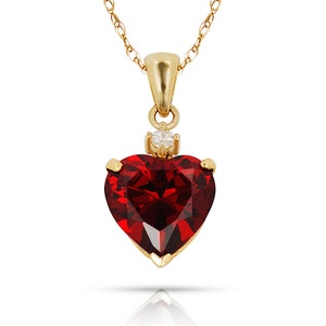 May include: A gold chain necklace with a heart-shaped pendant featuring a large red gemstone and a smaller clear gemstone at the top.