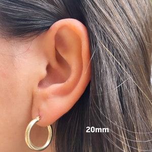 Puede incluir: Pendientes de aro de oro de 20 mm de di&aacute;metro. Los pendientes se muestran en la oreja de una persona.