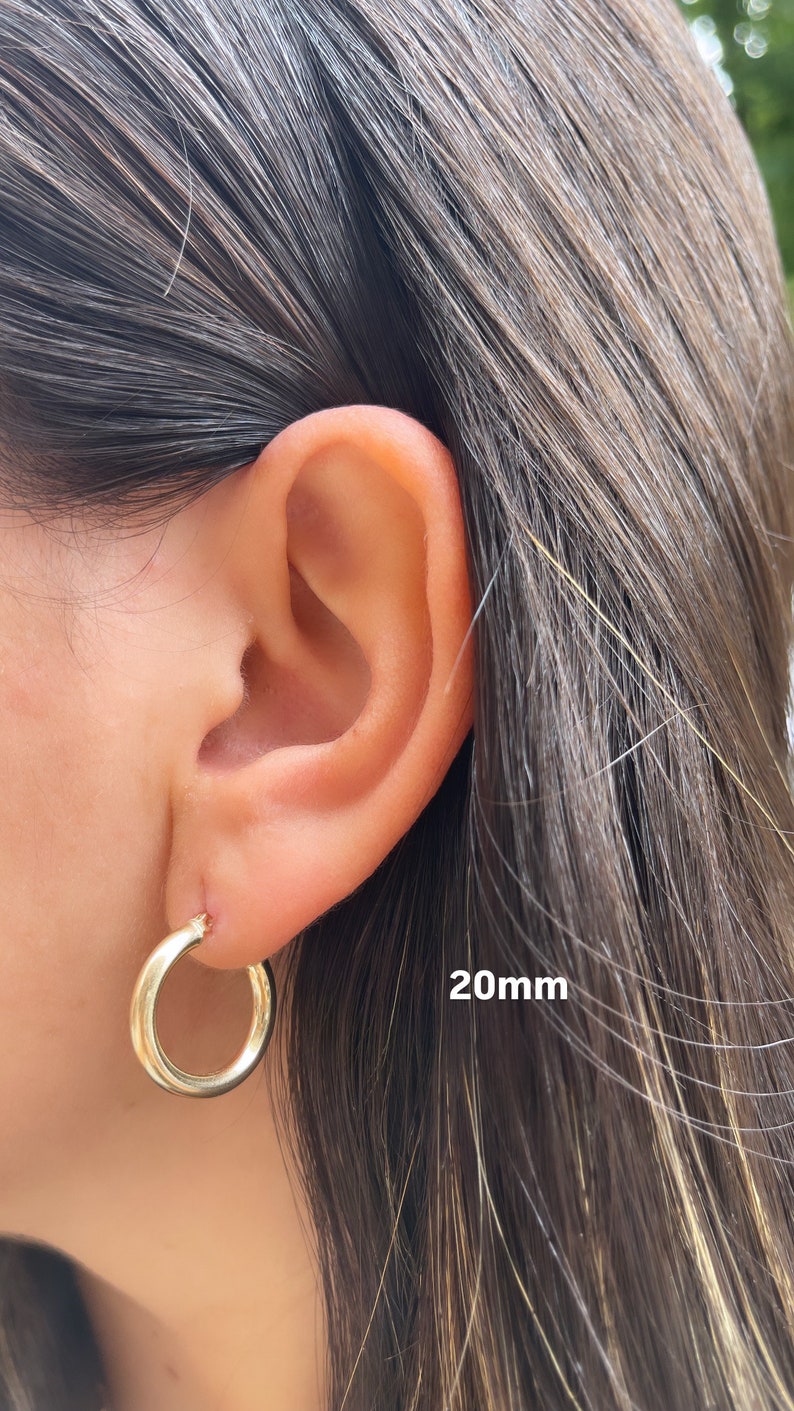 Puede incluir: Pendientes de aro de oro de 20 mm de di&aacute;metro. Los pendientes se muestran en la oreja de una persona.