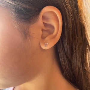 K&ouml;nnte beinhalten: Nahaufnahme eines Ohrs mit einem kleinen silbernen Schmetterlings-Ohrstecker.