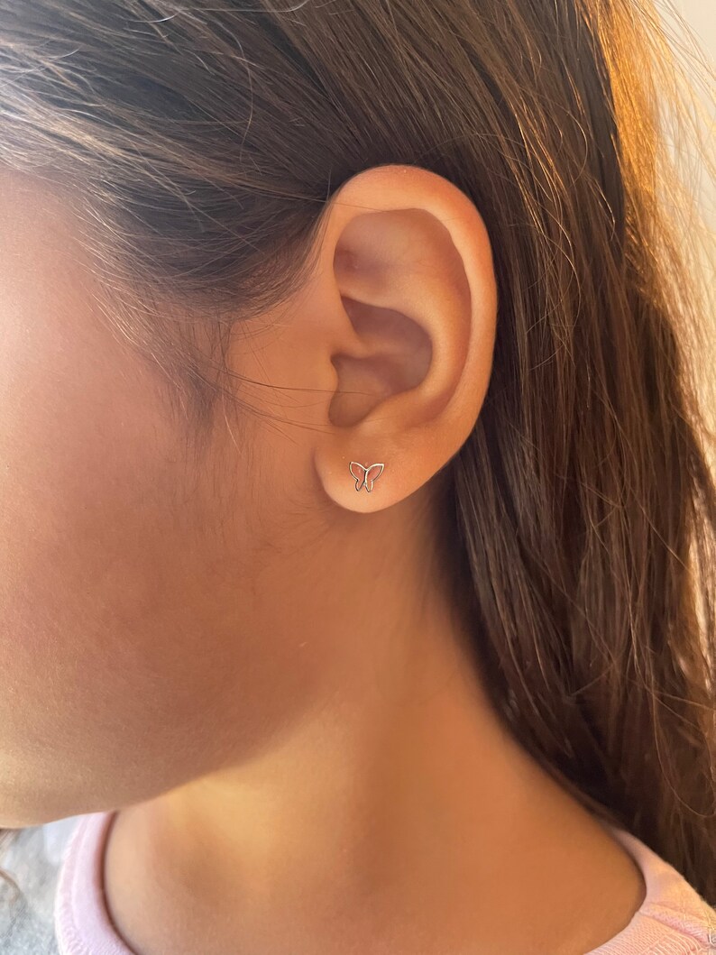K&ouml;nnte beinhalten: Nahaufnahme eines Ohrs mit einem kleinen silbernen Schmetterlings-Ohrstecker.