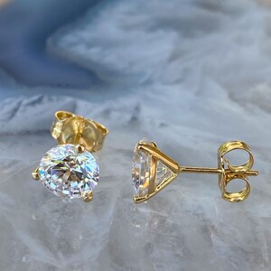 May include: A pair of gold stud earrings with a clear round and triangular shaped gemstone.