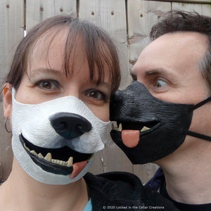 Puede incluir: Una pareja usando máscaras faciales con temática de perro. La mujer lleva una máscara blanca con una nariz negra y una lengua rosa. El hombre lleva una máscara negra con una lengua blanca. Las máscaras tienen un diseño realista de cara de perro.