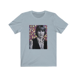 Puede incluir: Una camiseta azul claro con un estampado gr&aacute;fico de un hombre con cabello oscuro y un chaleco negro. El fondo del gr&aacute;fico es un patr&oacute;n colorido de rosa, amarillo y azul.