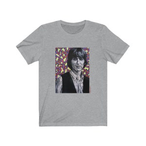 Puede incluir: Una camiseta gris con un gr&aacute;fico colorido de un hombre con cabello oscuro y un chaleco negro. El fondo del gr&aacute;fico es un patr&oacute;n colorido de rosa, morado, azul y amarillo.
