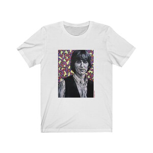 Puede incluir: Camiseta blanca con un estampado gr&aacute;fico colorido de un hombre con el pelo corto y oscuro. El gr&aacute;fico est&aacute; sobre un fondo de formas abstractas rosas, moradas, amarillas y naranjas.