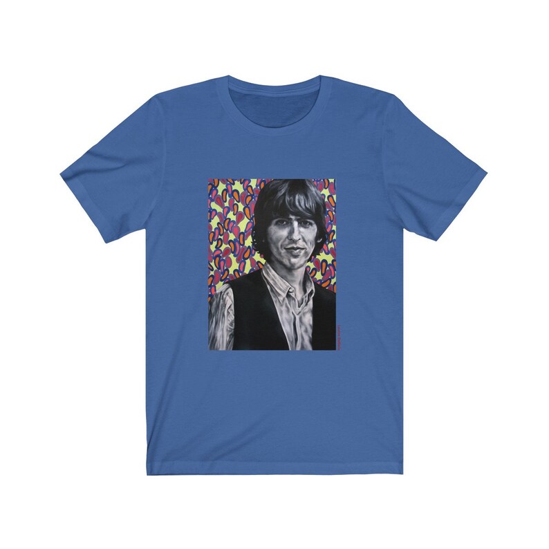 Puede incluir: Una camiseta azul con un gr&aacute;fico de un hombre con cabello oscuro y un chaleco negro. El fondo del gr&aacute;fico es un patr&oacute;n colorido de rosa, amarillo y azul.