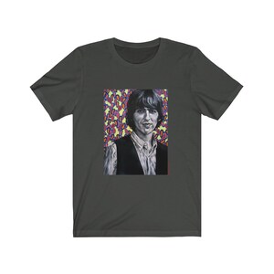 Puede incluir: Una camiseta verde oscuro con un retrato en blanco y negro de un hombre con cabello oscuro y un chaleco. El fondo es un patr&oacute;n colorido de rosa, morado, amarillo y naranja.