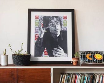 May include: A framed black and white portrait of a man with glasses, set against a colorful patterned background. The image is displayed on a wooden cabinet, alongside potted plants and a wire rack holding vinyl records.