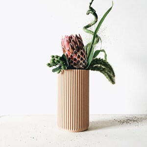 May include: A light brown, ribbed ceramic vase with a pink and green protea flower arrangement.