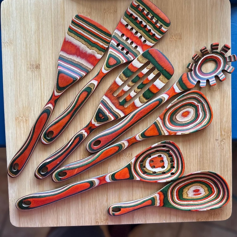 May include: Set of seven colourful wooden kitchen utensils with red, green and brown swirling patterns. The utensils include a spatula, a slotted spoon, a ladle, a whisk and a spoon with holes.