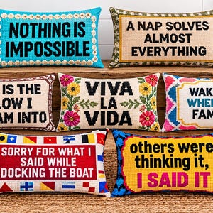 May include: Seven rectangular needlepoint pillows featuring various text designs. Top row: blue with 'NOTHING IS IMPOSSIBLE', beige with 'A NAP SOLVES ALMOST EVERYTHING'. Middle: beige with 'THIS IS THE PILLOW I SCREAM INTO', floral with 'VIVA LA VIDA', pink/blue with 'WAKE ME WHEN I'M FAMOUS'. Bottom: red with 'SORRY FOR WHAT I SAID WHILE DOCKING THE BOAT', yellow with 'others were thinking it, I SAID IT'.