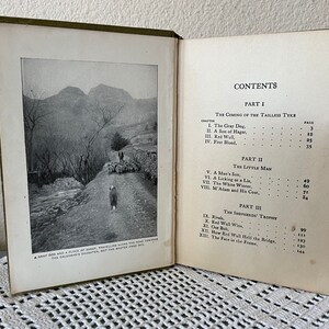 May include: Open book with a black and white landscape photo and text. The photo shows a dog and a flock of sheep on a road. The text on the right side lists the table of contents.