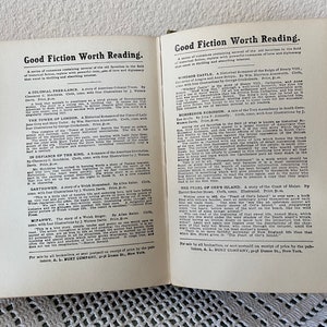 May include: Open book pages with text titled "Good Fiction Worth Reading." The text lists several book titles with descriptions. The pages are off-white with black text. The book is open on a light-colored surface.