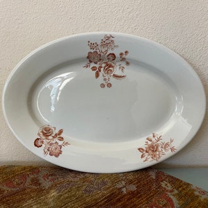 May include: Oval, white ceramic serving platter with a floral design in shades of brown. The platter features a glossy finish and is decorated with rose and other flower motifs. A classic piece for serving food.