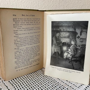 May include: An open book with a green cover and aged pages. The left page displays text, while the right page features a black and white illustration of two people in a room. The text reads "Bob, Son of Battle."