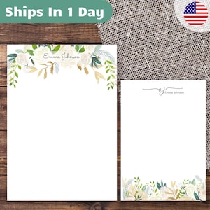 May include: Two white stationery sheets with floral designs. The larger sheet has a floral border at the top with the name "Emma Johnson" in script. The smaller sheet has a floral border at the bottom and the name "Emma Johnson" in script.